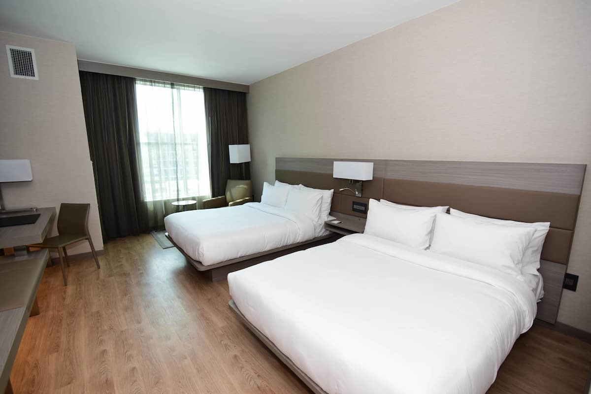 Ein Hotelzimmer mit zwei Betten, einem Schreibtisch, einem Stuhl und einem fenster mit Vorhängen.