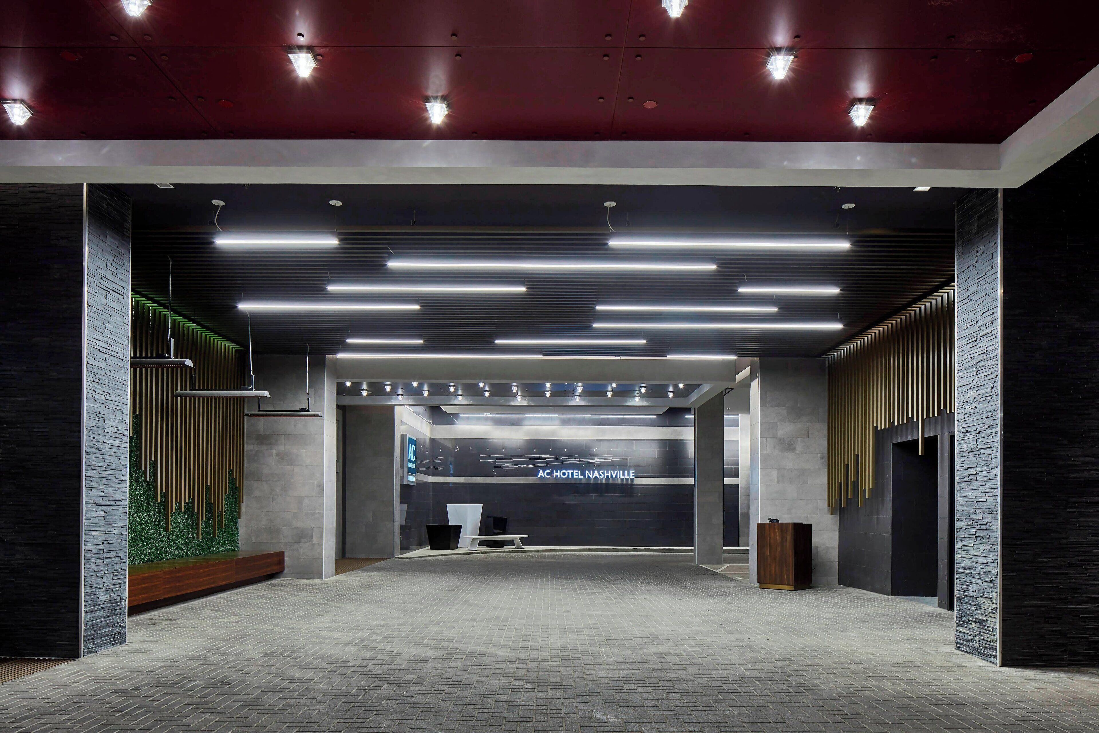 A modern hotel lobby with a reception desk, linear lighting, and a green wall feature.
