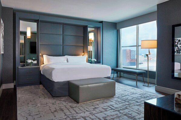 A modern hotel room with a large bed, a bench, a desk, and a view of the city through large windows. - AC Hotel by Marriott Nashville Downtown (Nashville)