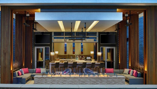 Un área de bar moderna al aire libre con asientos, una piscina y una chimenea.