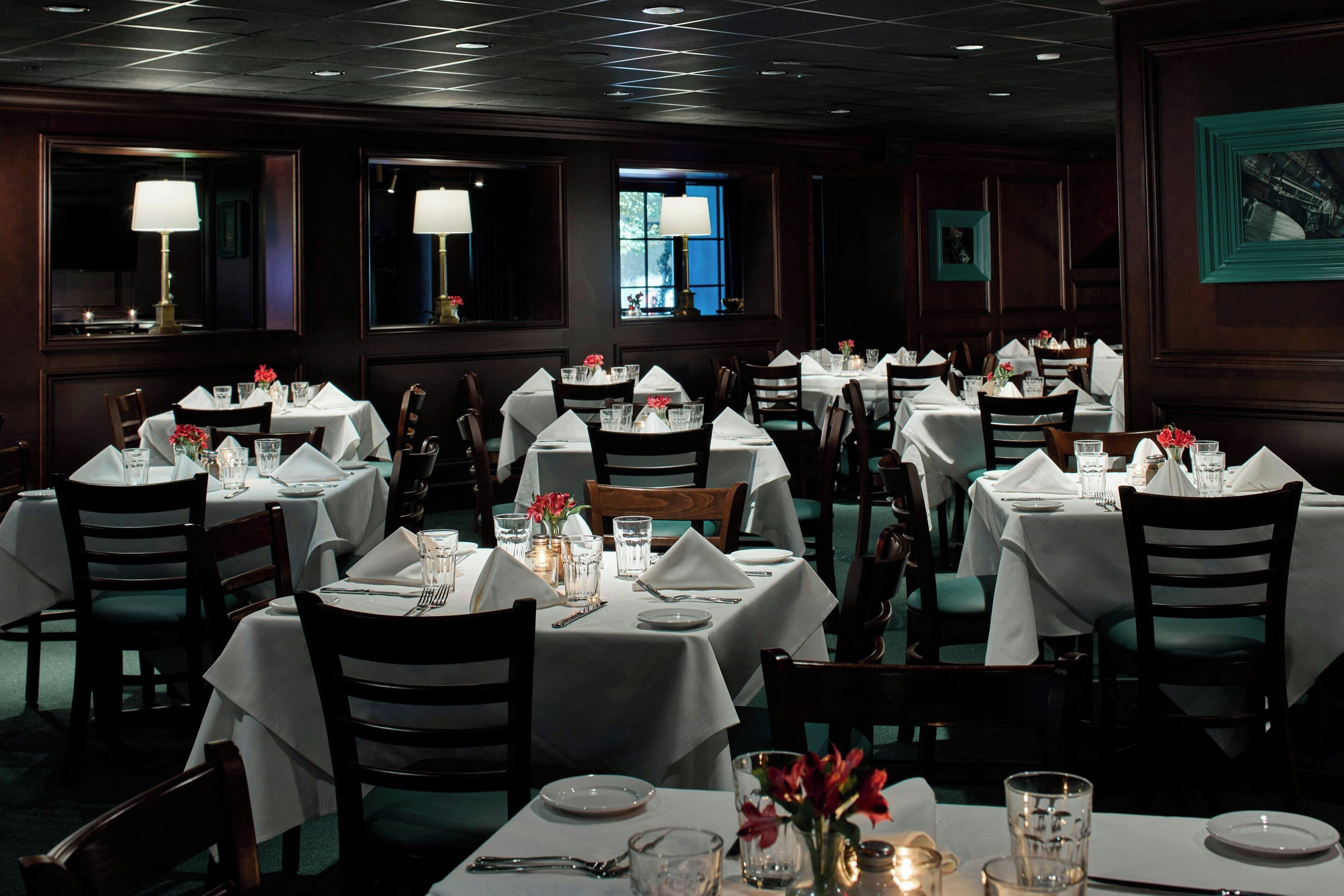 Une salle à manger élégante, avec plusieurs tables dressées pour le service, chacune étant recouverte d’une nappe blanche et agrémentée de chaises.