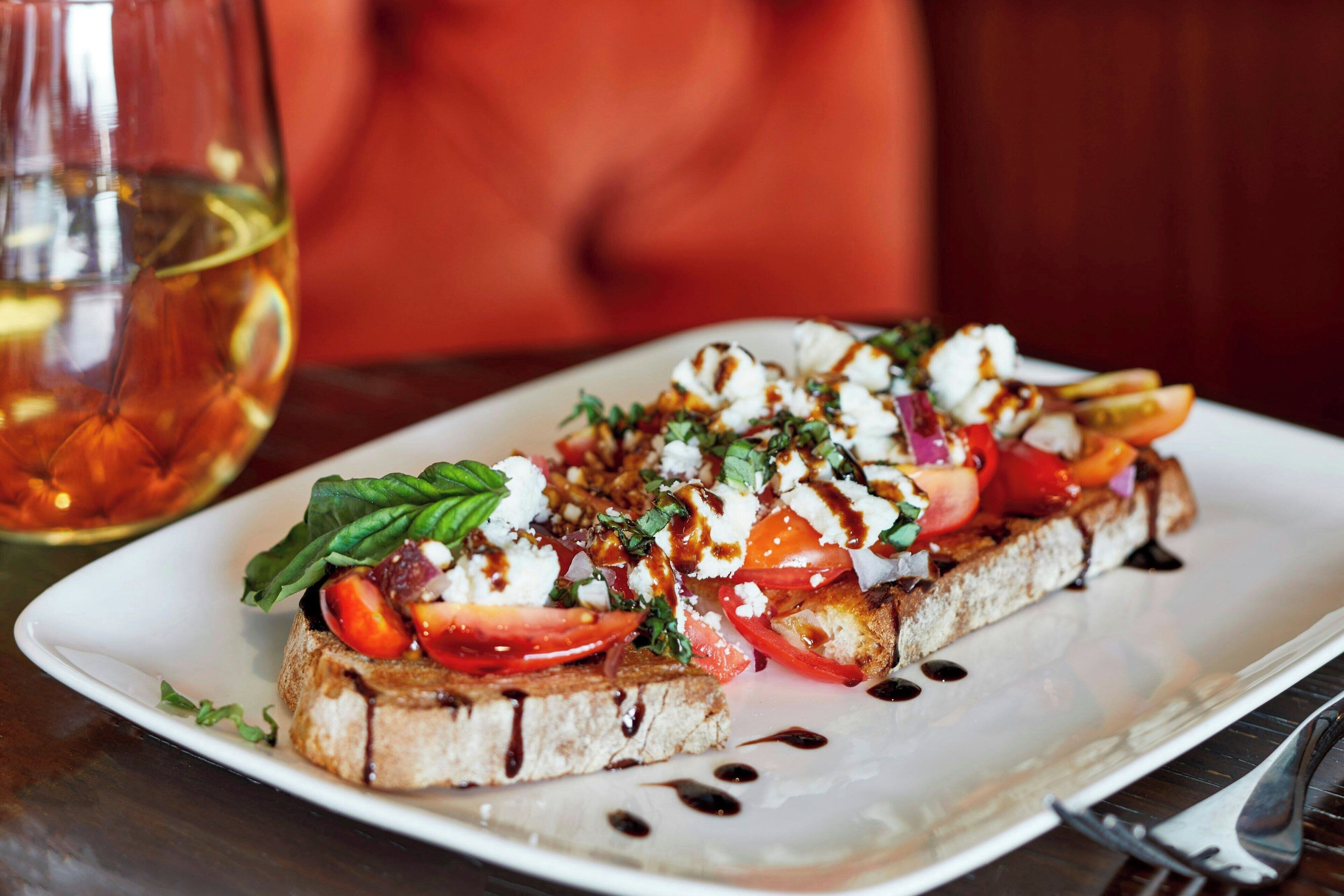 A plate of bruschetta with tomatoes, basil, and mozzarella on a white plate.