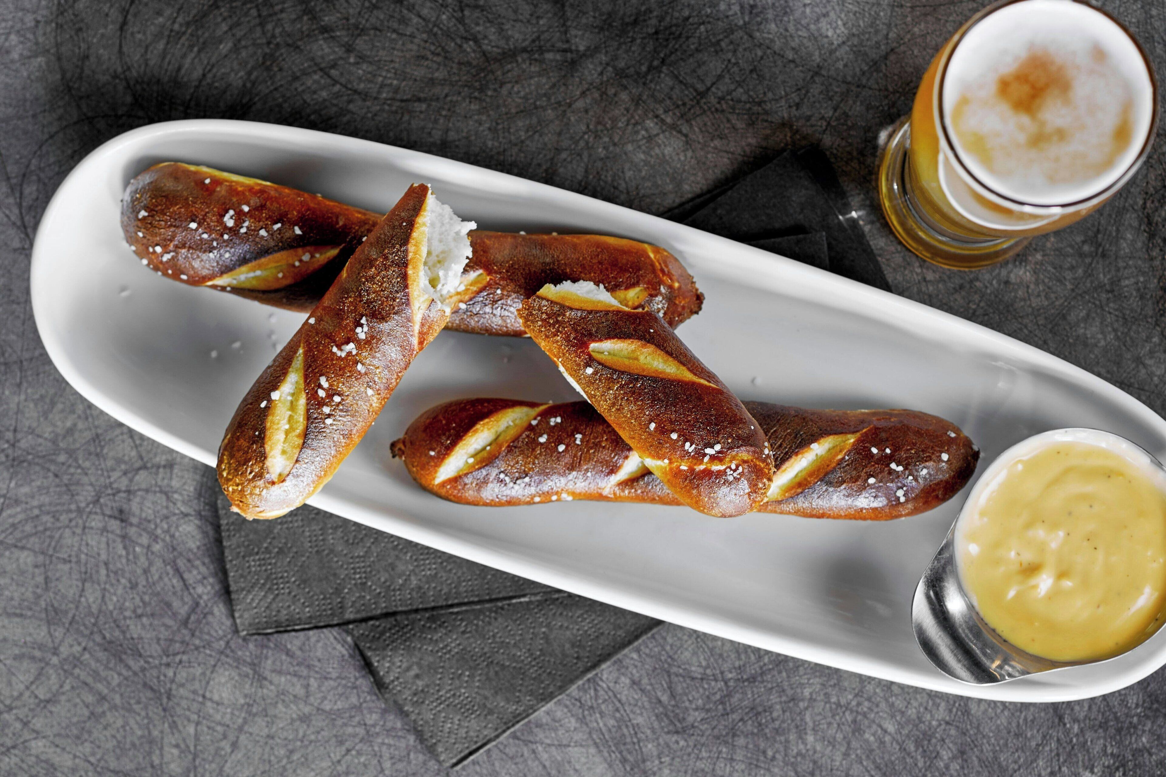 Um prato branco com pretzels e uma pequena tigela de mostarda.
