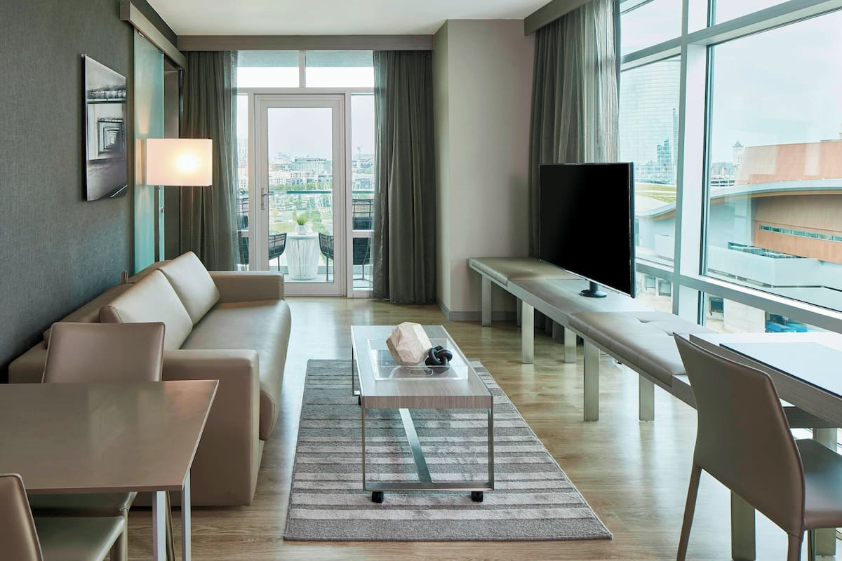 Ein modernes Hotelzimmer mit Sofa, Esstisch, Fernseher und Blick auf die Stadt.