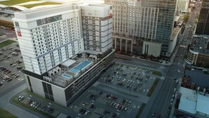 Un hotel moderno con piscina en la azotea, varios niveles de estacionamiento y un patio central.