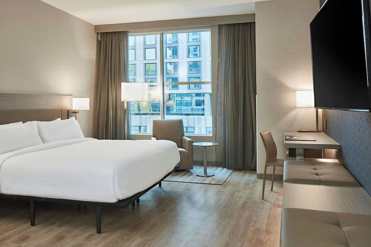 Ein Hotelzimmer mit einem großen Bett, einem Schreibtisch mit Stuhl, einem kleinen runden Tisch und einem Fernseher.