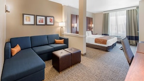 Habitación de hotel con sofá modular, cama, escritorio y un amplio ventanal con cortinas.