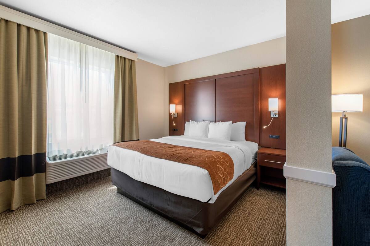 Hotelkamer met een groot bed, nachtkastje, twee wandlampen, raam met gordijnen en een wandradiator.