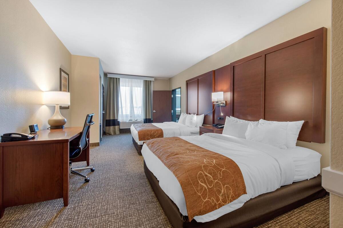 Een hotelkamer met twee bedden, een bureau, een stoel, een lamp en een raam met gordijnen.
