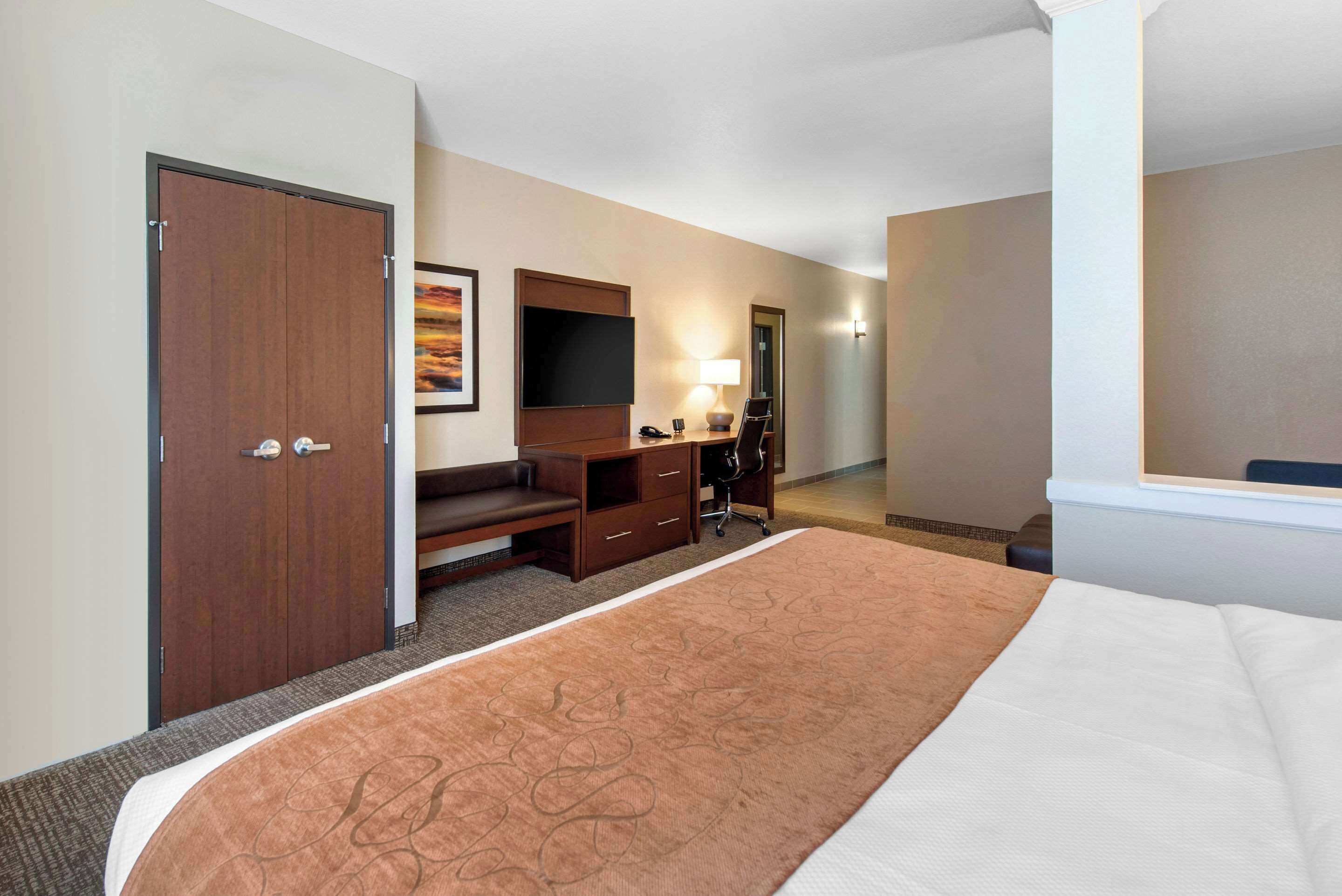 A hotel room with a bed, a desk with a chair, a television, and a wardrobe.