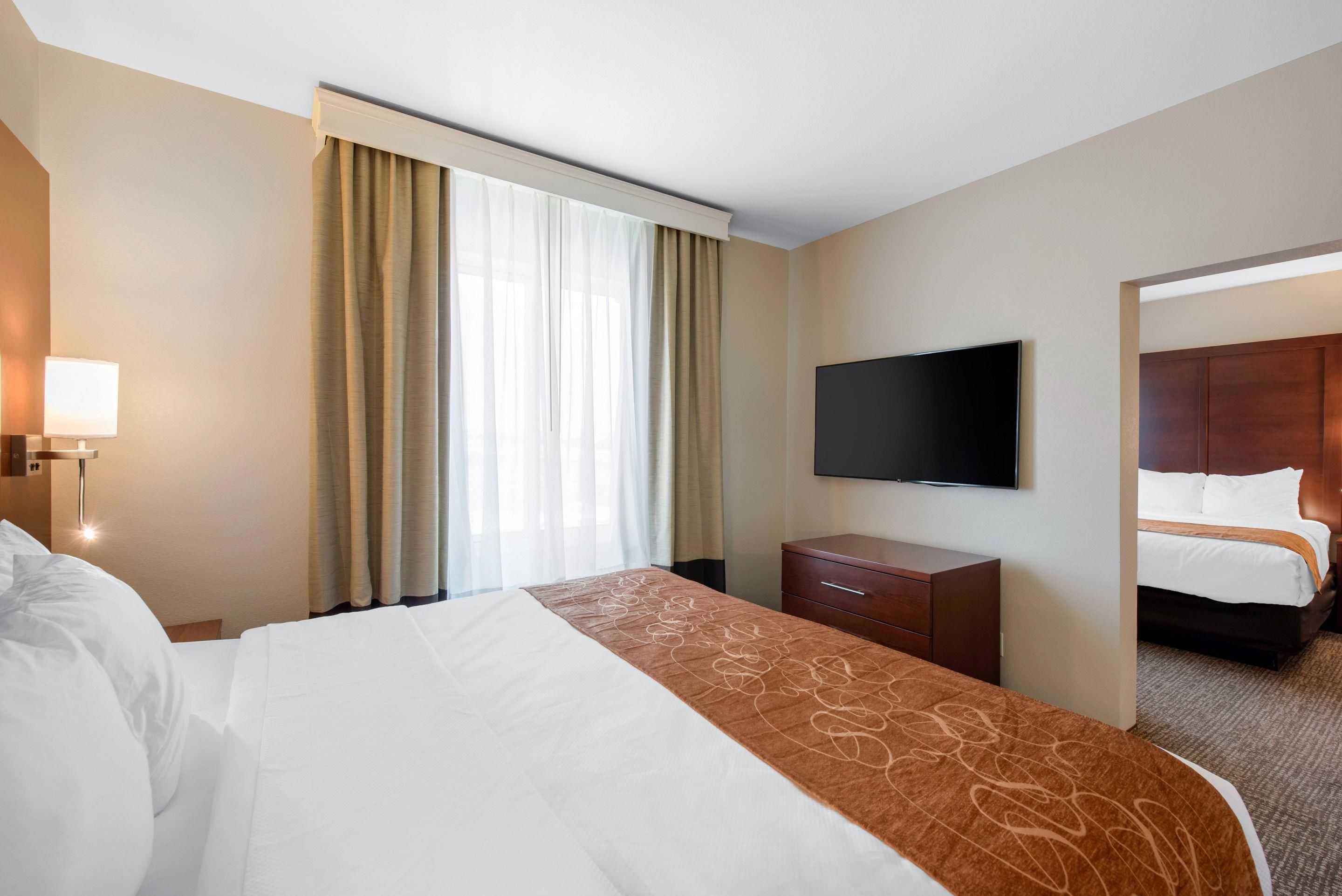 Habitación de hotel con una cama grande, un televisor de pantalla plana en la pared, un escritorio con lámpara y una ventana con cortinas.