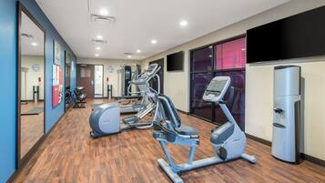 A gym with cardio machines, a water dispenser, and a mirror on the wall.