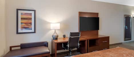 A hotel room with a bed, a desk with a chair, a TV, a lamp, and a framed picture on the wall.