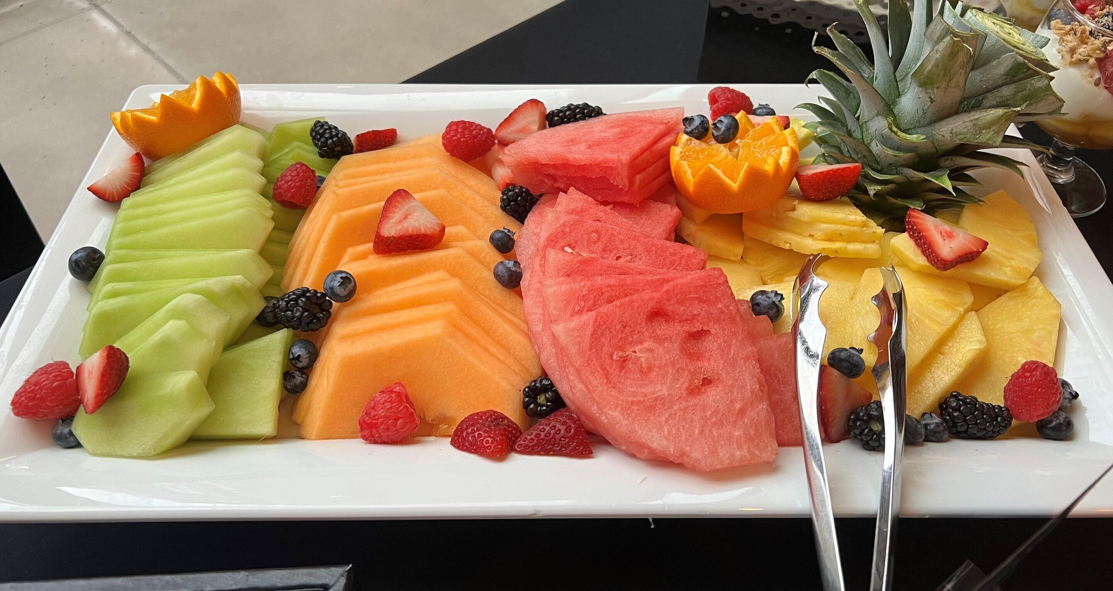 A rectangular white tray with various fruits including watermelon, cantaloupe, pineapple, strawberries, and blueberries.