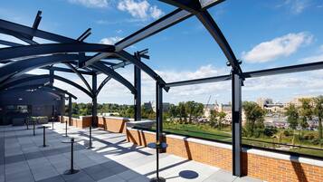 An outdoor terrace with a clear view of the cityscape, featuring a modern architectural design with metal beams and a brick wall.