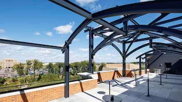 An outdoor terrace with a metal roof structure, brick walls, and a view of a parking lot and buildings in the background.
