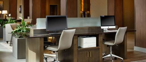 A modern hotel lobby with a reception desk, two computer workstations, comfortable seating, and a decorative plant.