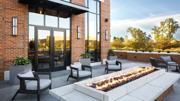 Une terrasse extérieure dotée d’un foyer, de sièges et d’un bâtiment en briques avec de grandes fenêtres.