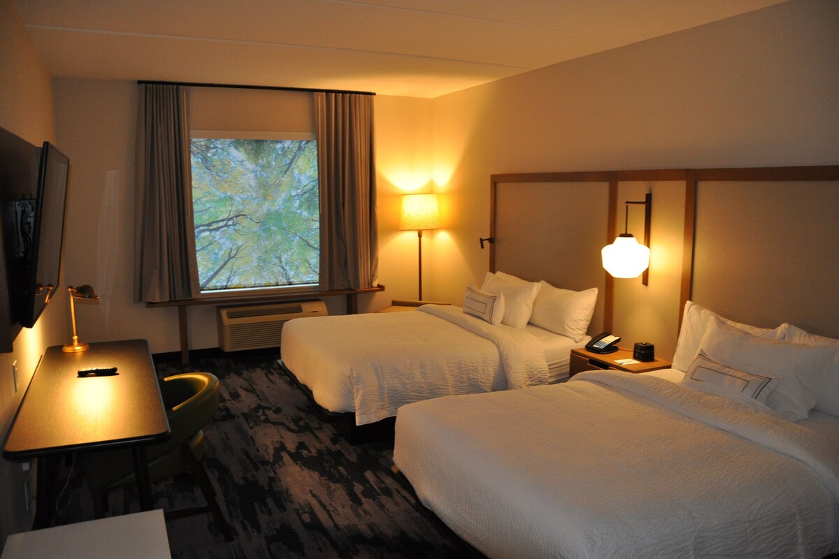 A hotel room with two beds, a desk, a chair, a TV, and a window with curtains.