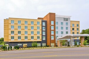 Un hotel de varios pisos con un diseño moderno, que presenta una combinación de fachadas amarillas y marrones, y una entrada destacada con un corredor cubierto.