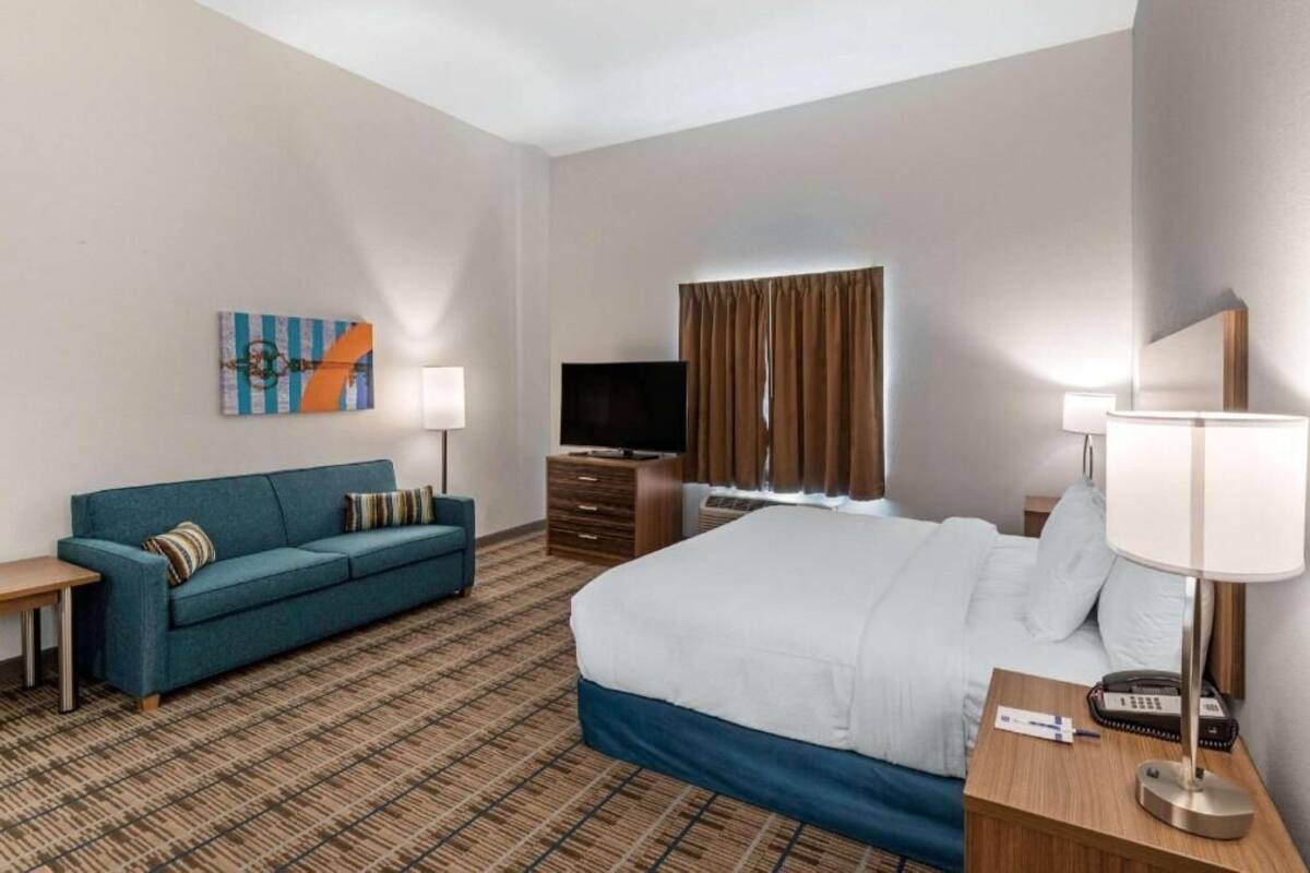 A hotel room with a bed, a sofa, a TV, a lamp, and a painting on the wall.