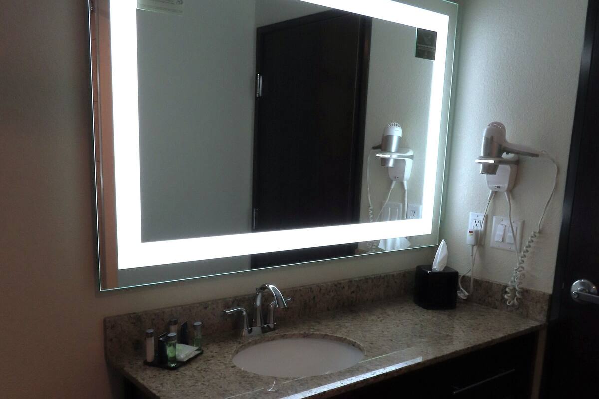 A hotel bathroom with a large mirror, a sink, a hairdryer, and a towel rack.