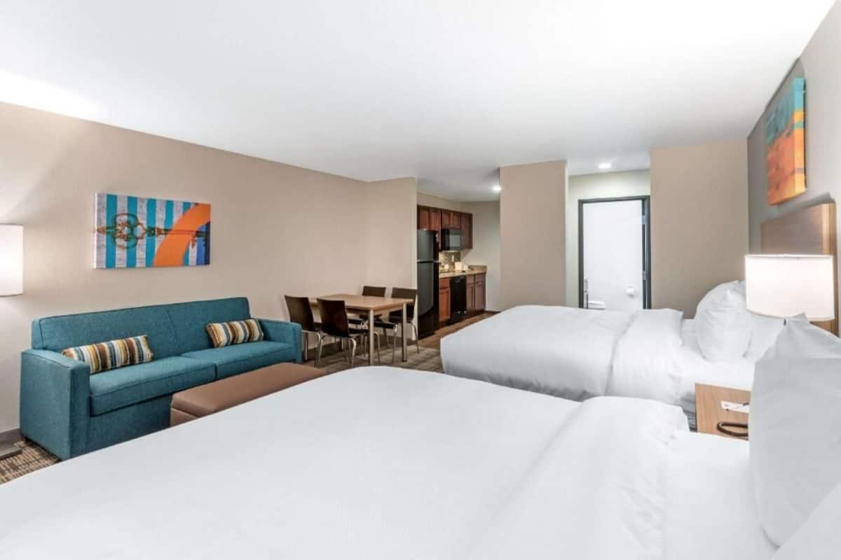 A hotel room with two beds, a sofa, a dining table, and a kitchenette.