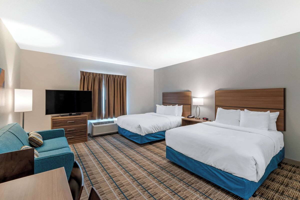 A hotel room with two beds, a TV, a desk, and a sofa.