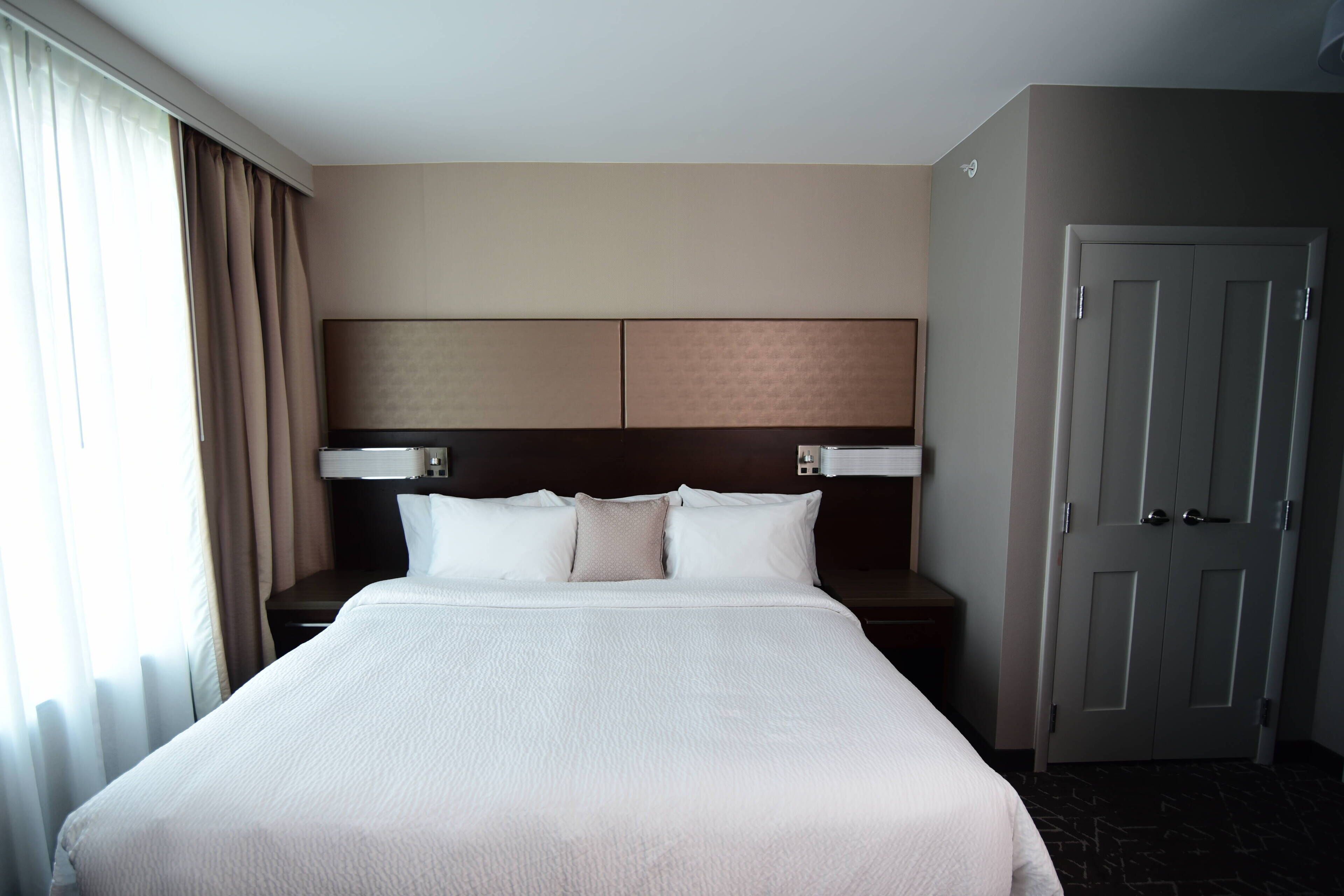 A hotel room with a large bed, a headboard, a nightstand, and a door.