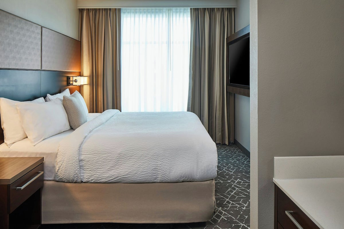 Una habitación de hotel con una cama grande, televisión, escritorio y ventana con cortinas.