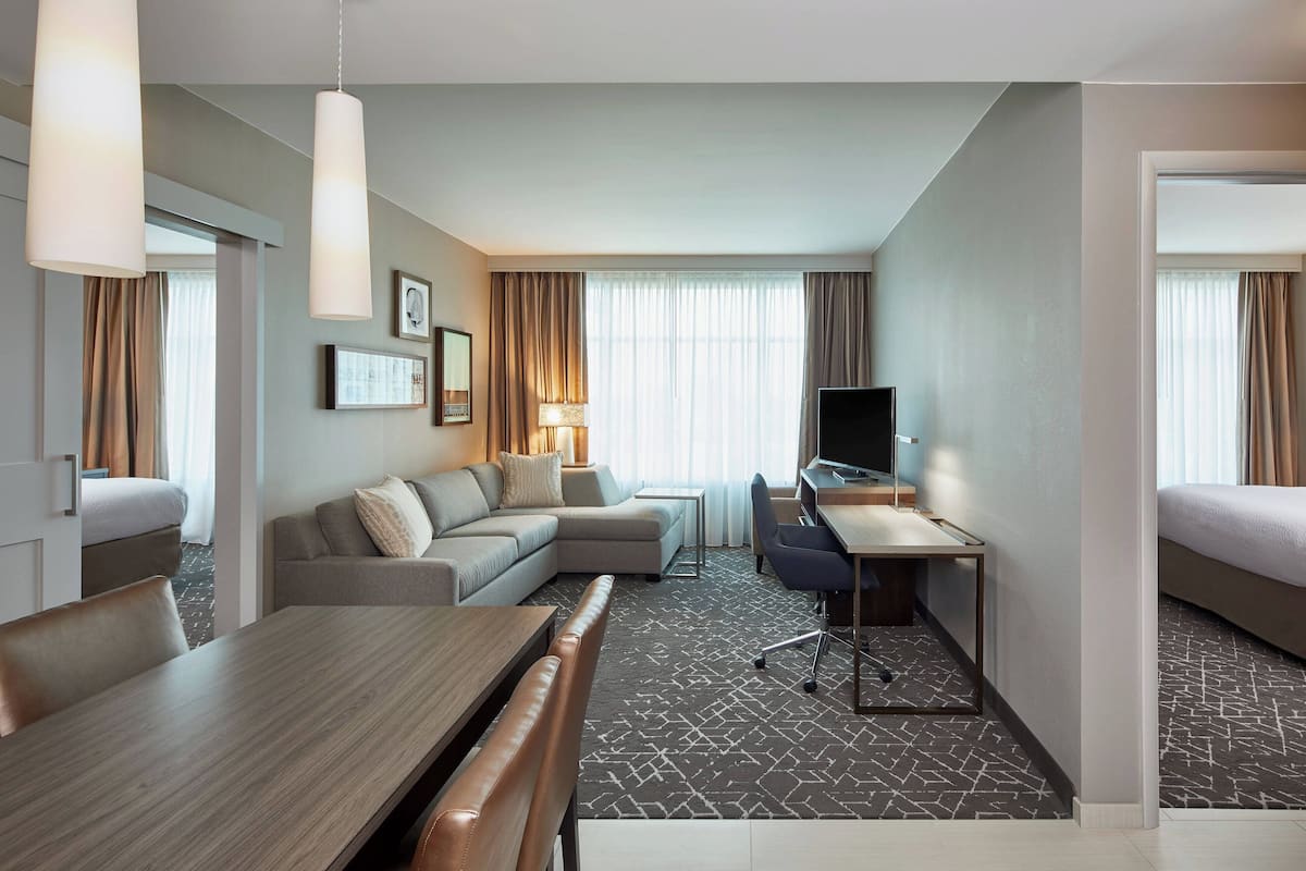 Una habitación de hotel moderna con zona de comedor, sofá, televisión y cama.