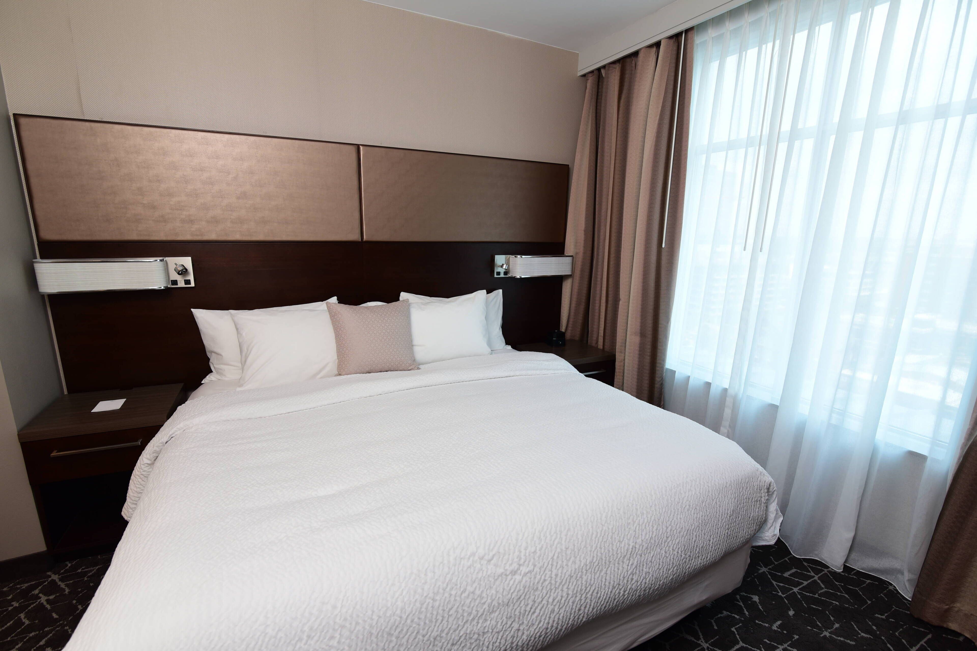 A hotel room with a large bed, a headboard, a nightstand, and a window with curtains.