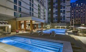 Ein Poolbereich auf dem Dach mit mehreren Pools, Liegestühlen und einer Bar.