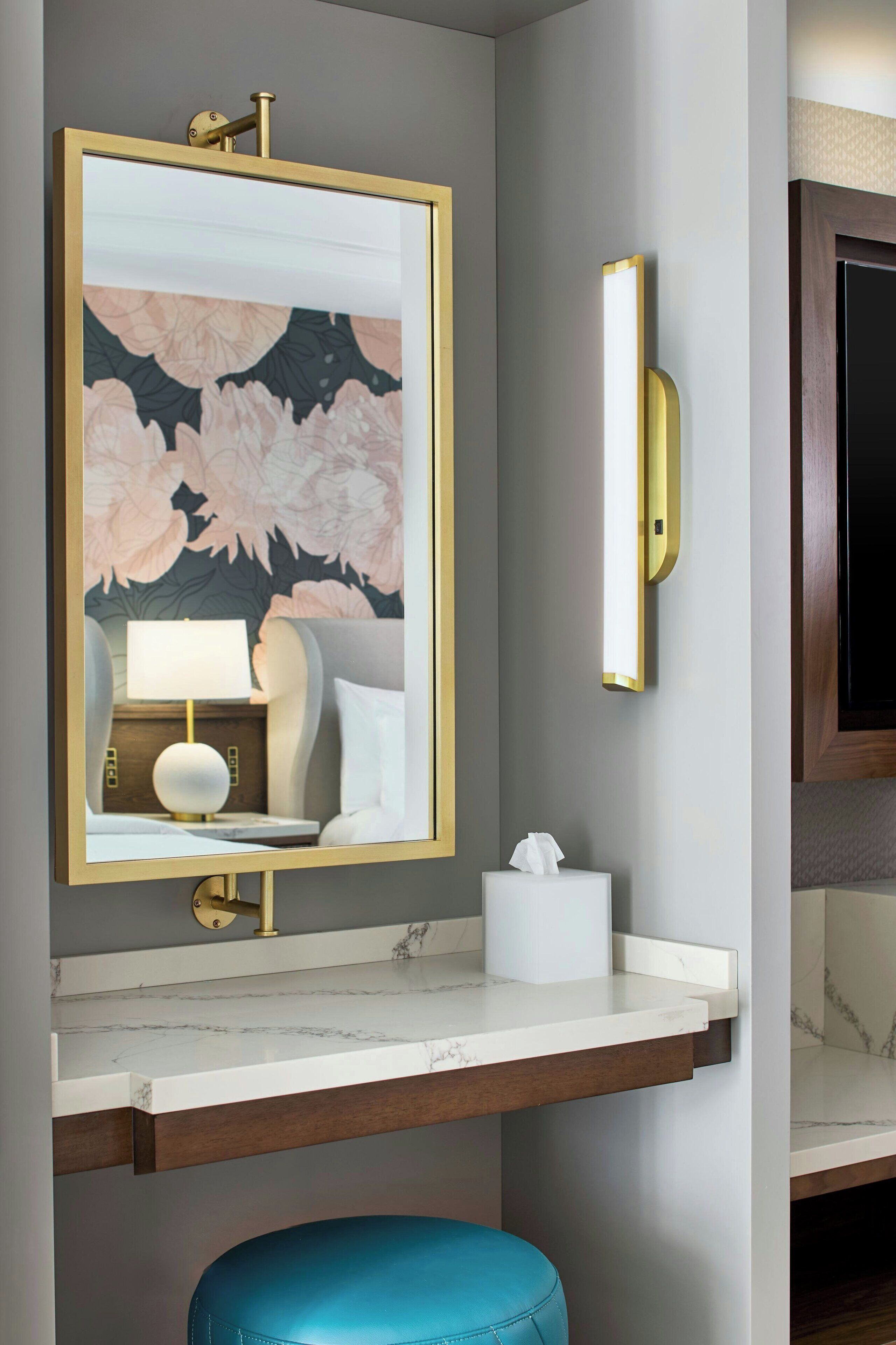 A bathroom with a marble countertop, a gold-framed mirror, a blue stool, and a tissue box.
