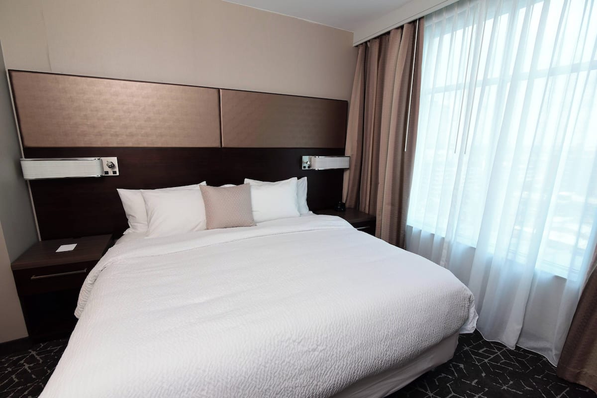 Una cama grande con cabecera, mesita de noche y ventana con cortinas.
