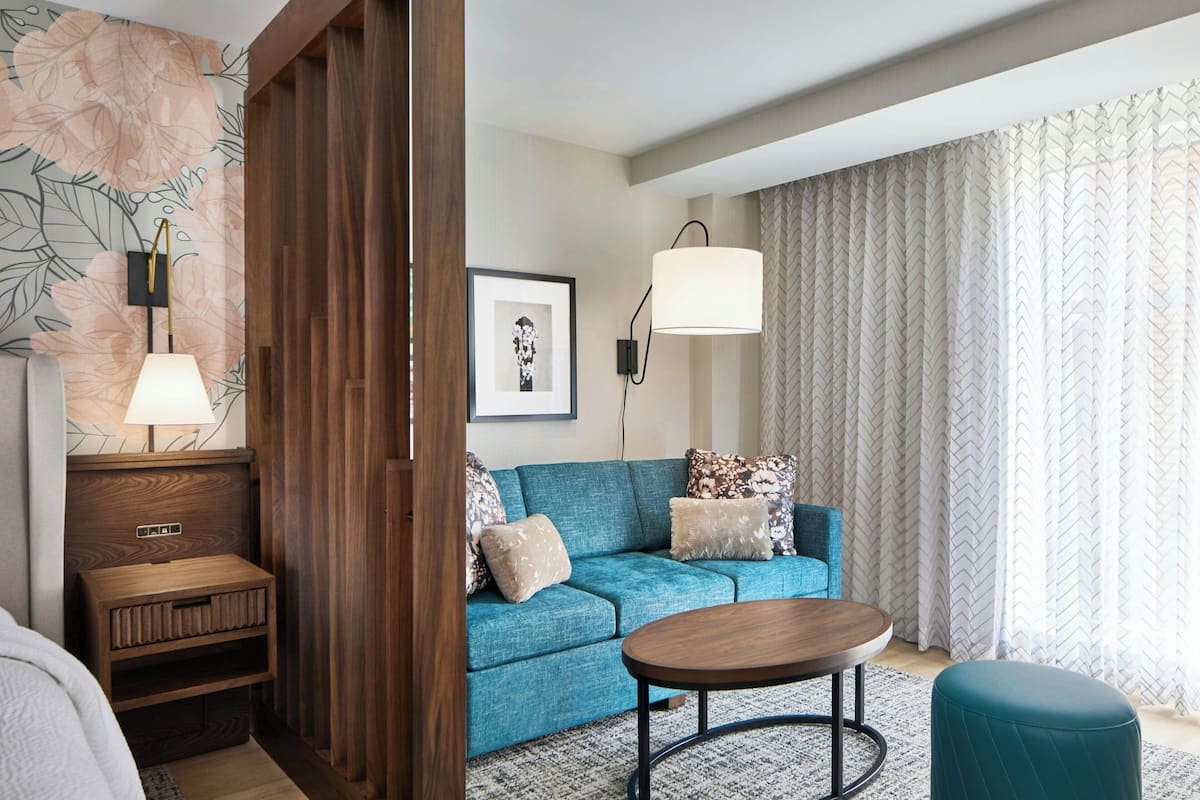 Un salón moderno con un sofá azul, una mesa de centro de madera, una mesita auxiliar y una lámpara.
