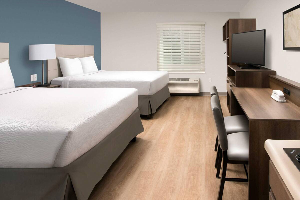Ein Hotelzimmer mit zwei Betten, einem Schreibtisch, einem Fernseher und einem Fenster mit Jalousien.