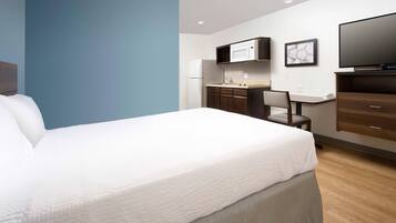 A hotel room with a large bed, a desk with a chair, a microwave, a refrigerator, and a flat-screen TV.