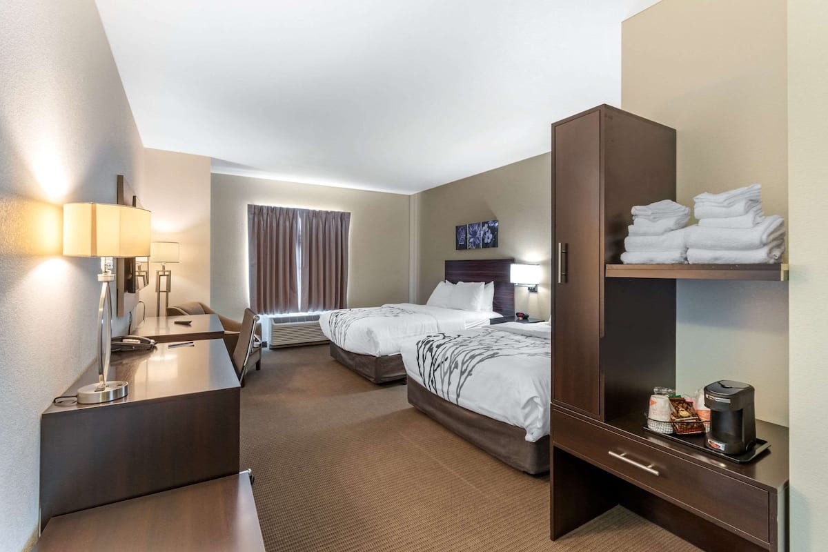 Ein Hotelzimmer mit zwei Betten, einem Schreibtisch, einem Kleiderschrank und einer Kaffeemaschine.