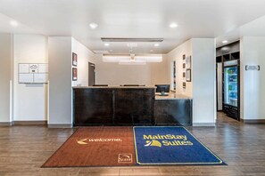 A hotel reception area with a reception desk, a coffee machine, a refrigerator, and a welcome mat.