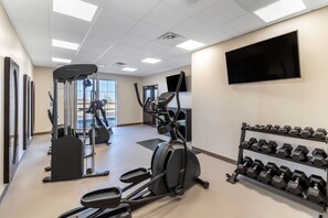 A gym with cardio machines, dumbbells, and a TV on the wall.