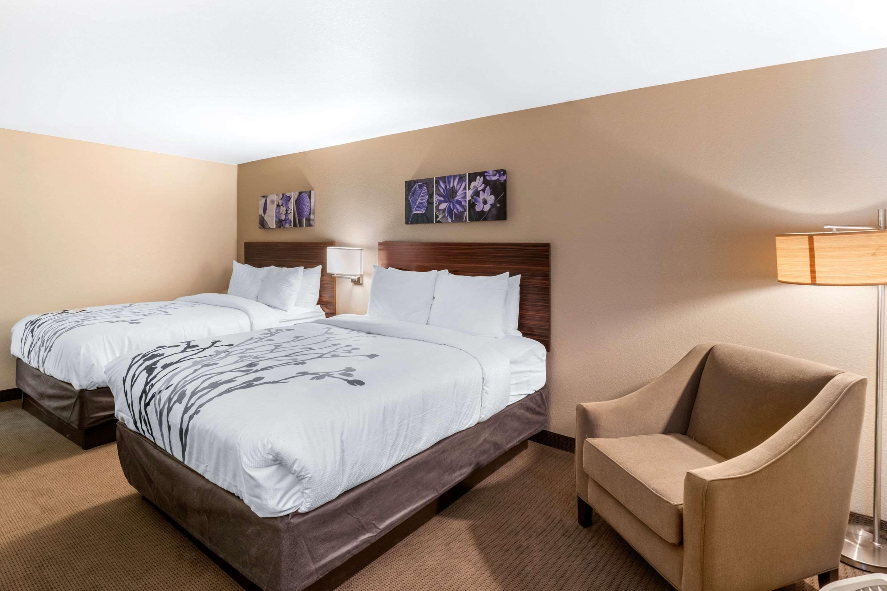 Una habitación de hotel con dos camas, una silla y obras de arte en las paredes.
