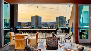 Un bar moderno en la azotea con vistas a la ciudad, que cuenta con varias zonas de estar e iluminación con luces colgantes.
