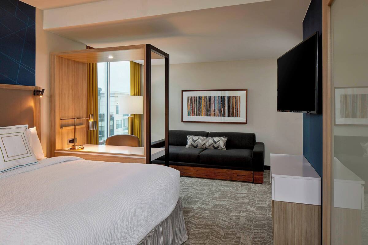 Une chambre d’hôtel avec un grand lit, un bureau, un canapé, une télévision et une fenêtre donnant sur des immeubles.