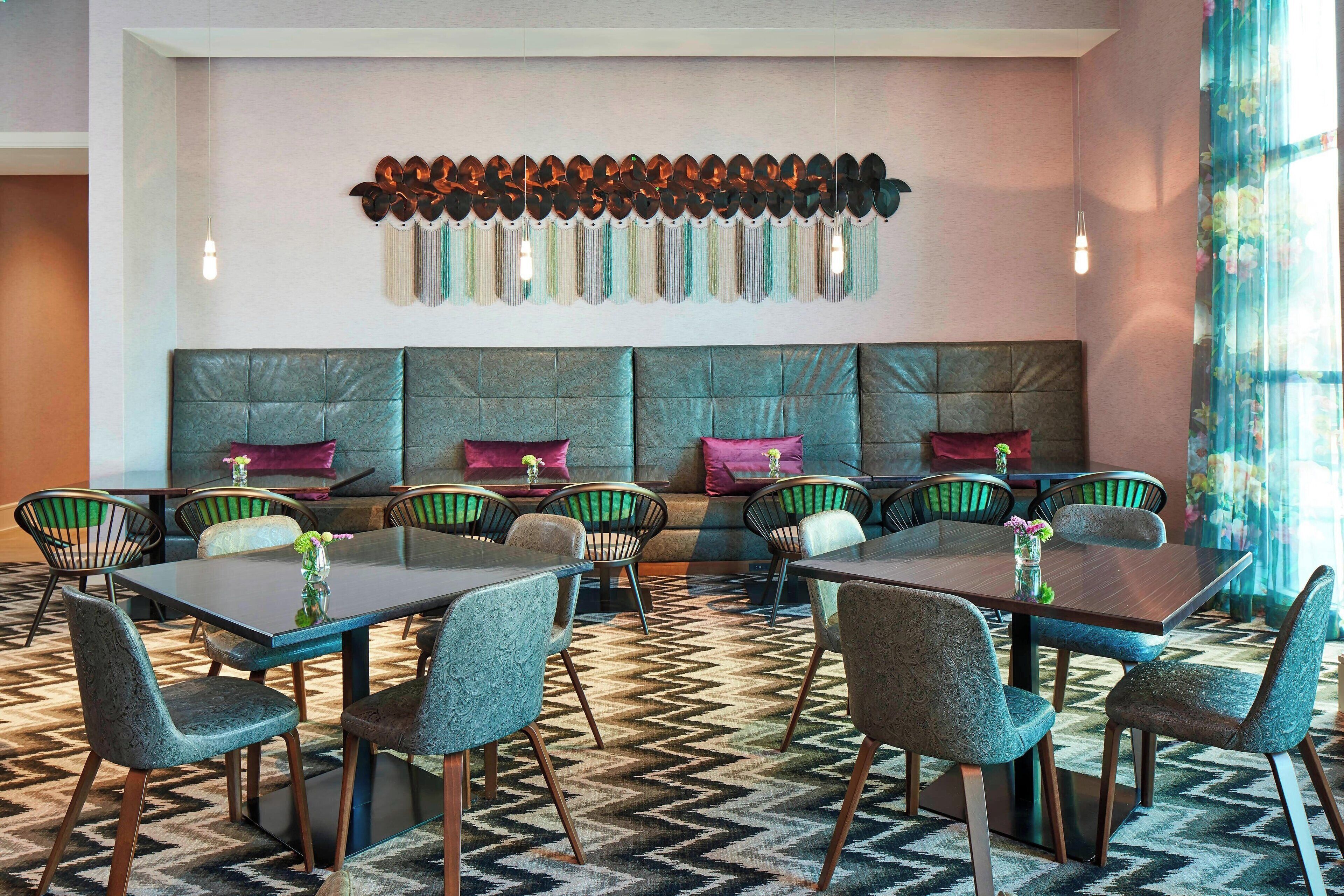 A modern dining area with a long table and chairs, a patterned carpet, and a decorative wall piece.