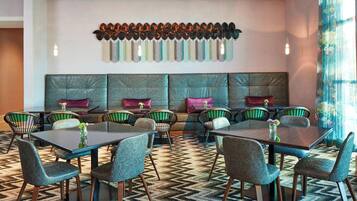 A modern dining area with a long table and chairs, a patterned carpet, and a decorative wall piece.