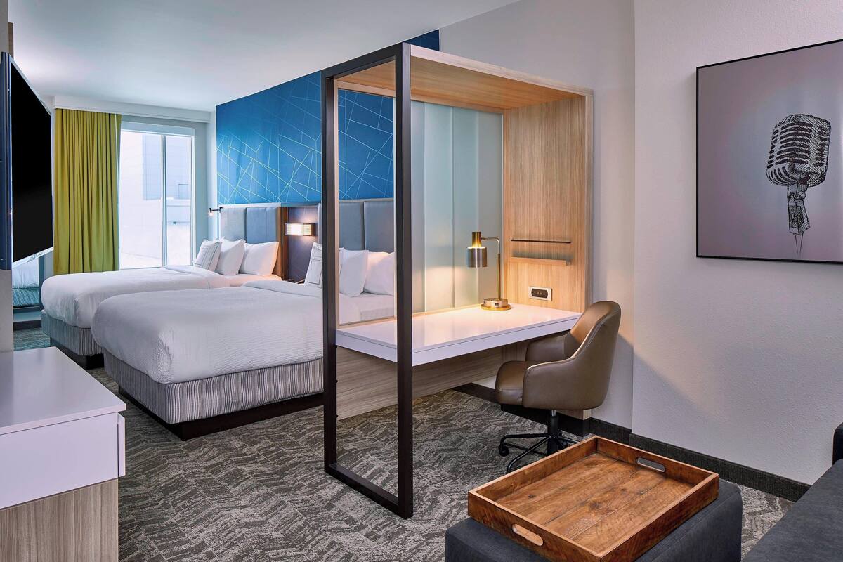 Une chambre d’hôtel avec deux lits, un bureau, une chaise et une grande fenêtre.