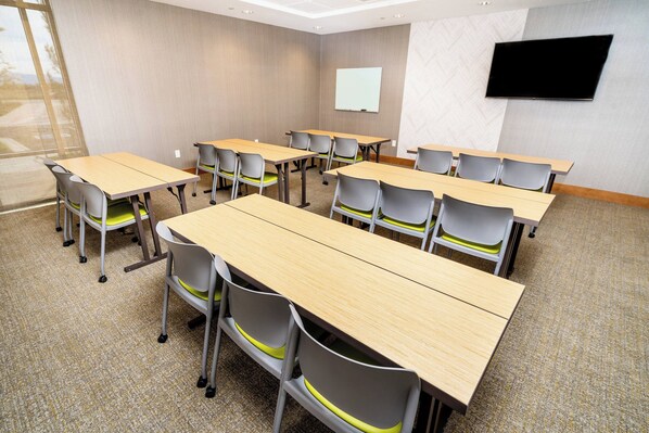 Un salón de conferencias con varias mesas y sillas, una pizarra y un televisor en la pared.