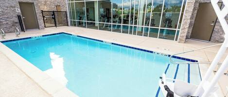 Una piscina con cerramiento de vidrio, una silla de salvavidas y una puerta a la derecha.