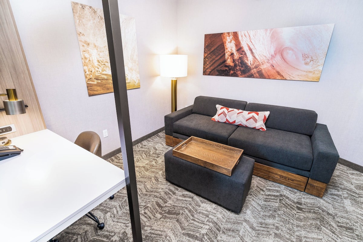 Ein modernes Wohnzimmer mit grauem Sofa, einem Holztisch, einem weißen Schreibtisch und einer Lampe.